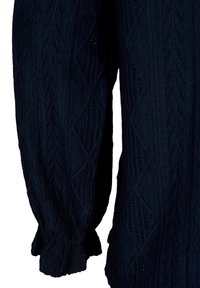 Pantalon long en maille texturée bleu foncé avec motifs losanges et torsades et poignets ajustés aux chevilles.