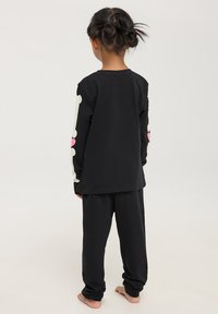 Set di pigiama in cotone nero con maniche lunghe e grafiche colorate di ossa e cuori. Vestibilità rilassata con pantaloni a vita elastica, tessuto morbido.