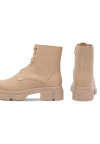 Beżowe skórzane botki za kostkę z sznurowanym przodem, okrągłym noskiem i grubą teksturowaną podeszwą. Posiadają minimalne przeszycia i zamek błyskawiczny z tyłu.