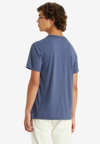 Camiseta de algodón azul con mangas cortas y cuello redondo, que presenta una sutil textura jaspeada y una pequeña etiqueta de marca cerca del dobladillo.
