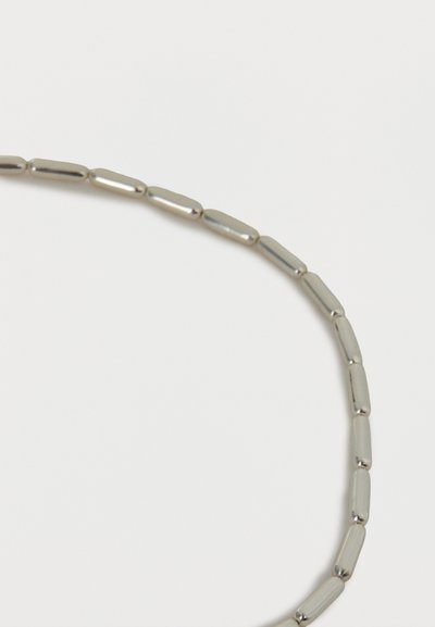 Ασημένιο κολιέ με επιμηκυσμένες κυλινδρικές χάντρες, τοποθετημένες σε καμπύλη γραμμή σε λευκό φόντο.