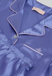 Satenasta pižama iz sivke s kontrastnim svetlo roza robom, ovratnikom z zarezami, zapiranjem na gumbe, elastičnim pasom in vezenim žepnim detajlom.