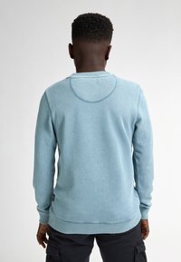 Felpa azzurra chiara con maniche lunghe, scollo a girocollo e polsini a costine. Presenta una texture morbida e un leggero motivo mélange.
