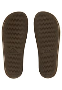Semelles de sandales en caoutchouc brun avec un motif de rainure en vagues et le logo Quiksilver, présentant une texture lisse et mate ainsi que des bords arrondis.