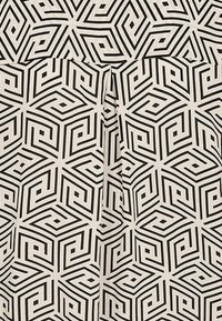 Motivo geometrico nero su un tessuto beige, caratterizzato da forme quadrate interconnesse e linee, con una texture liscia e dettagli di piega.