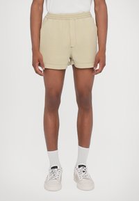 Helle beige Shorts mit einem elastischen Bund, Seitentaschen und lockerer Passform. Getragen mit weißen Socken und helle Sneakers.