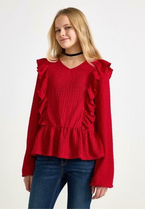 Rød tekstureret top med volangærmer og peplum talje. V-halsdesign med lange ærmer, parret med blå jeans. Choker-accessoire inkluderet.