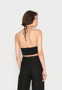 Top cropped preto com alças halter e bainha desfiada, emparelhado com calças pretas de cintura alta com bolsos traseiros e um tecido texturizado.