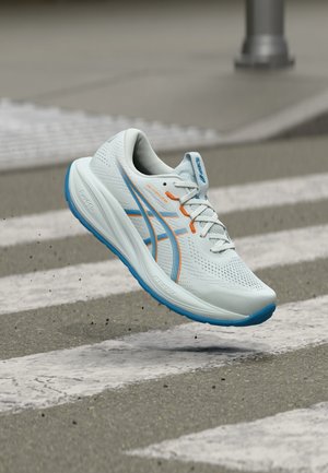 Weißer und blauer Laufschuh mit orangefarbenen Akzenten, in der Luft über einem Fußgängerüberweg schwebend, mit detaillierter Sohle und atmungsaktivem Obermaterial aus Mesh.