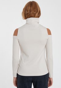 Helles beige Langarmshirt mit hohem Kragen und Kalt-Schulter-Design. Glatte Stoffqualität mit schmaler Passform.
