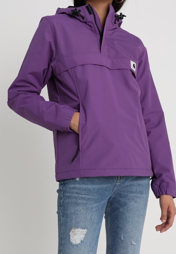 Lilla pullover-jakke med hætte, forlommelomme med lynlås, elastiske manchetter og snorejusteringer. Kombineret med slidte blå jeans.