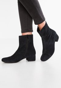 Botines de ante negros con puntera cuadrada y tacón bajo. Cuentan con una cremallera externa en un lado y una textura suave.