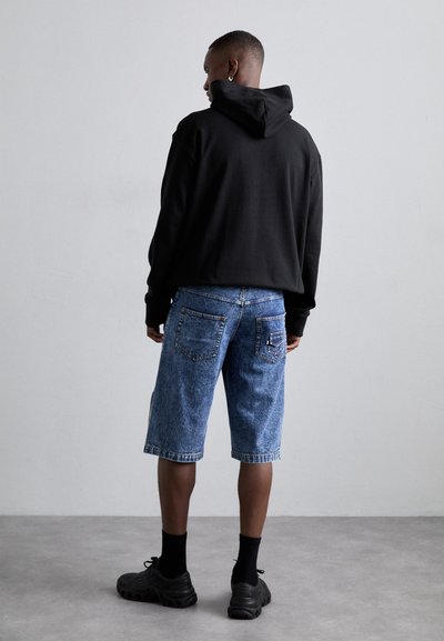 Black hooded sweatshirt, blue denim shorts, above the knee. Shorts feature back pockets and contrast stitching. Black sneakers complete the look.