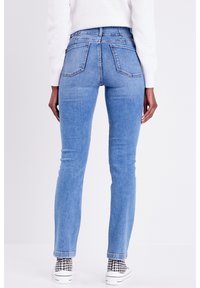 Jean skinny en denim bleu avec une taille haute, dotée de poches arrière et d'une texture lisse. Associés à des baskets blanches et des chaussettes à motifs.