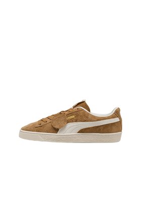 Zapatilla de ante marrón con franja blanca de Puma, suela beige, cierre con cordones y detalle de llavero circular de ante unido en el lateral.