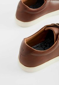Bruine leren sneakers met een gladde afwerking, crèmekleurige rubberen zolen, inzetsels met bloemmotief en gestikte details aan de achterkant.