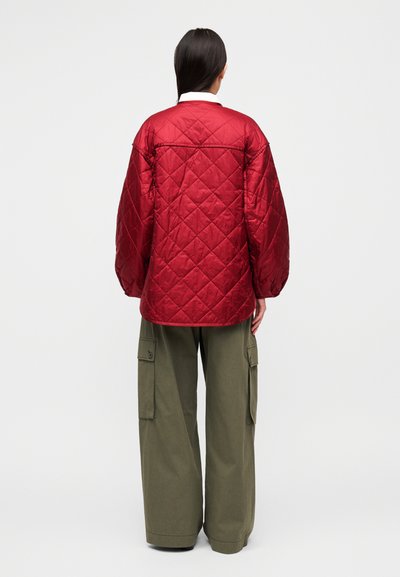 Κόκκινο μπουφάν με καπιτονέ ύφασμα, φαρδιά μανίκια, σχεδιασμό με στρώσεις και γιακά. Συνδυάζεται με άνετο χακί cargo παντελόνι με πλαϊνές τσέπες.