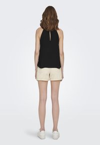Top negro sin mangas con detalle de escote en la espalda, combinado con pantalones cortos color crema. La tela parece suave con un corte holgado. Zapatillas blancas completan el atuendo.