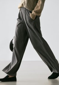 Pantalon gris plissé à jambes larges avec un design formel, doté d'une taille haute et de fines rayures. Associé à des mocassins noirs et un petit sac.