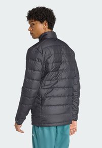 Black puffer jacket with horizontal quilted design and high collar. Worn with teal pants. Features smooth texture and lightweight material.