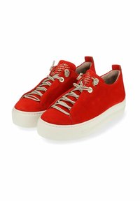 Baskets en suede rouge avec un bout rond, lacets beiges et semelle en caoutchouc blanche. La languette présente un texte imprimé dans une couleur contrastante.