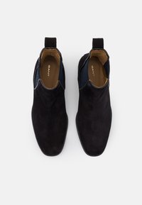 Černé semišové kotníkové boty s elastickými bočními panely, poutkem a hladkým koženým interiérem. Elegantní, zužující se design pro dokonale padnoucí vzhled.