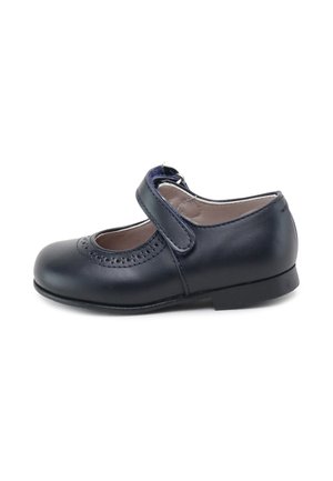 Zapato Mary Jane de cuero negro para niñas con patrón decorativo perforado y cierre de velcro sobre fondo blanco.