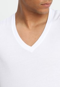 Hvit V-hals T-skjorte laget av myk bomullsstoff med glatt tekstur og minimalistisk design, med en klassisk utringning og tettsittende fasong.
