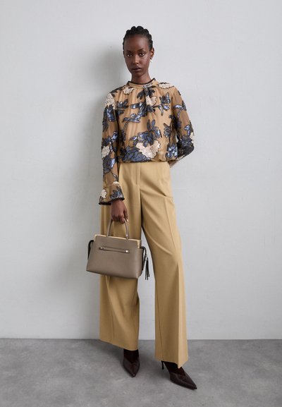 Blouse fluide à fleurs en beige avec des accents bleus, large pantalon beige et sac à main taupe, associés à des escarpins marron à bout pointu.