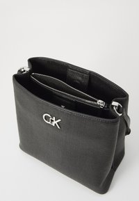 Borsa nera texturizzata con hardware in argento e un logo evidente, dotata di un compartimento con zip e un ampio interno.