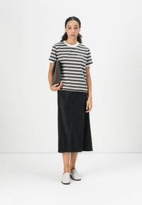 Stribet kortærmet t-shirt i mørkegrøn og hvid, sammen med en sort satin midi-nederdel og lysegrå slip-on sko. Holder en sort clutch.