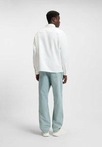 Hvid skjorte med lange ærmer og klassisk krave, parret med lyseblå denim jeans. Sættet har en afslappet pasform og sømløst bagdesign.