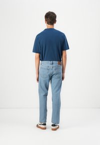 Marineblauwe t-shirt met korte mouwen en ronde hals, gecombineerd met lichtblauwe rechtvallende jeans en witte sneakers met zwarte accenten.