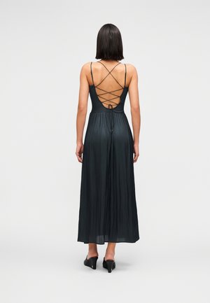 Abito maxi nero con corpetto aderente e schiena scoperta caratterizzata da cinturini incrociati. Tessuto fluido, plissettato e leggermente lucido, abbinato a tacchi neri.