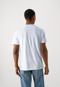 T-shirt en coton blanc avec un col rond et des manches courtes, présentant une texture lisse et une coupe décontractée. La vue de dos ne montre aucun motif ni accent.