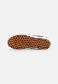 Semelle de sneaker en caoutchouc avec un motif en losange, présentant une surface marron et des bords blancs. Inclut un accent rose sur le dessus.