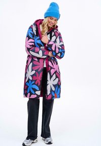 Barevný dlouhý kabát s květinovým vzorem v růžové, modré a bílé barvě. Vyroben z lehkého materiálu, s kapucí a předním zipem.