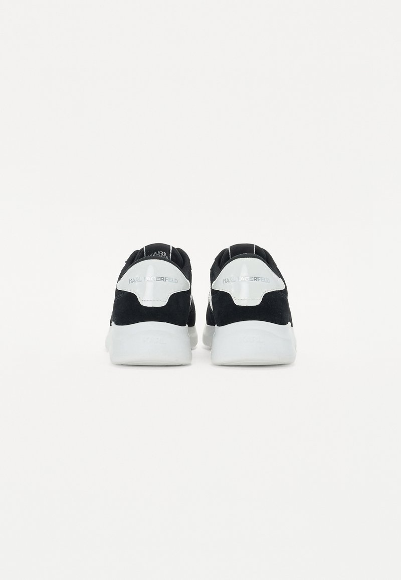 Baskets en suède noir avec des semelles en caoutchouc blanc, arborant un design minimaliste, un talon courbé et des accents de logo à l'arrière.