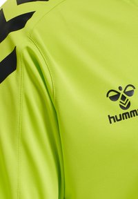 Felgroen sportshirt gemaakt van gladde stof. Bevat zwarte chevronstrepen op de schouders en een zwart logo-opdruk op de voorkant.