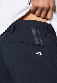 Σκούρο μπλε παντελόνια με υφή υφάσματος, κομψό σχεδιασμό, ρίγες στο π λάι και λευκό λογότυπο στην πίσω τσέπη.