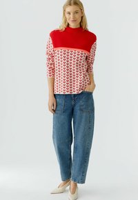 Rot-weiß gemusterter Pullover mit Dreiviertelärmeln, kombiniert mit hellblauen Baggy-Jeans. Weiße spitz zulaufende Schuhe runden den Look ab.