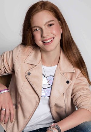 Rosa Kunstwildlederjacke, weißes T-Shirt mit Pailletten-Lippen, schichtweise Halsketten, silberne und rosa Armbänder sowie eine silberne Uhr am Handgelenk des Models.