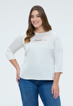 Top bianco a maniche lunghe con scollo rotondo, con la scritta "Positive feeling" in corsivo nero sul petto. Tessuto liscio.