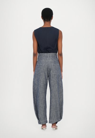 Top senza maniche blu navy con vita arricciata e chiusura con zip; abbinato a pantaloni ampi in stile denim con tasche posteriori e vestibilità rilassata.