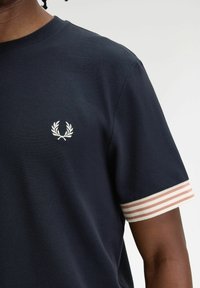Polo a maniche corte blu navy con tessuto testurizzato, caratterizzato da un'emblema bianco sul petto e accenti a righe rosa chiaro sulle maniche.