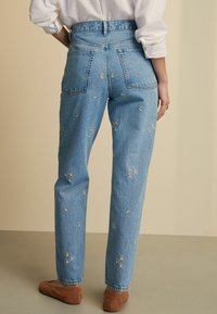 Vaqueros de mezclilla azul claro con bordado de flores, corte recto, cintura alta, cinco bolsillos y un acabado ligeramente texturizado.