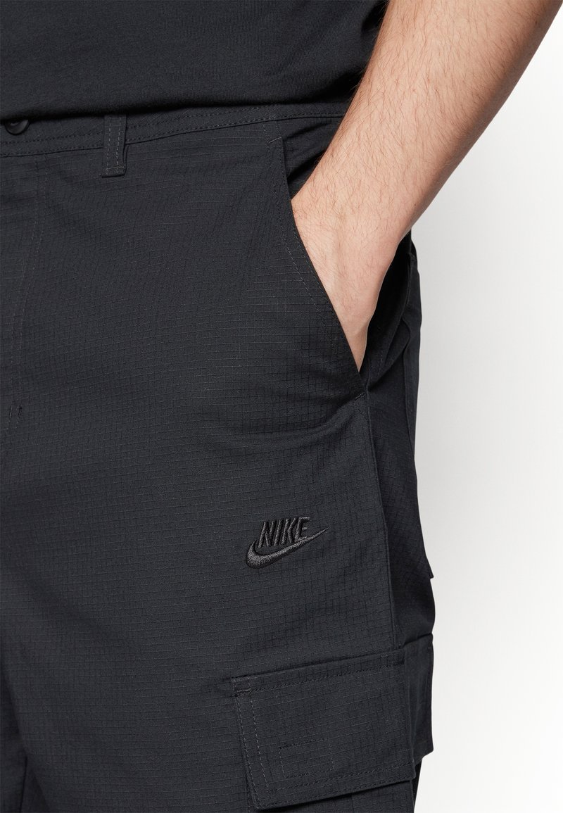 Shorts cargo Nike en noir, avec un tissu texturé, des poches latérales et un petit logo brodé sur la poche gauche.