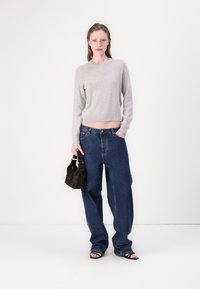 Maglione grigio chiaro a maglia con orlo a costine, abbinato a jeans in denim blu a vita alta e larghi. Modella che tiene in mano una piccola borsa nera, indossando sandali neri.