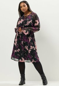 Svart blommig klänning med rosa och lila intrikata mönster, långa ärmar, knytkrage och utsvängd silhuett, matchad med svarta ankelstövlar.