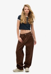 Pantalones anchos marrones con detalles de costura clara, combinados con una camiseta corta azul marino con ribete blanco. Unas zapatillas completan el look.